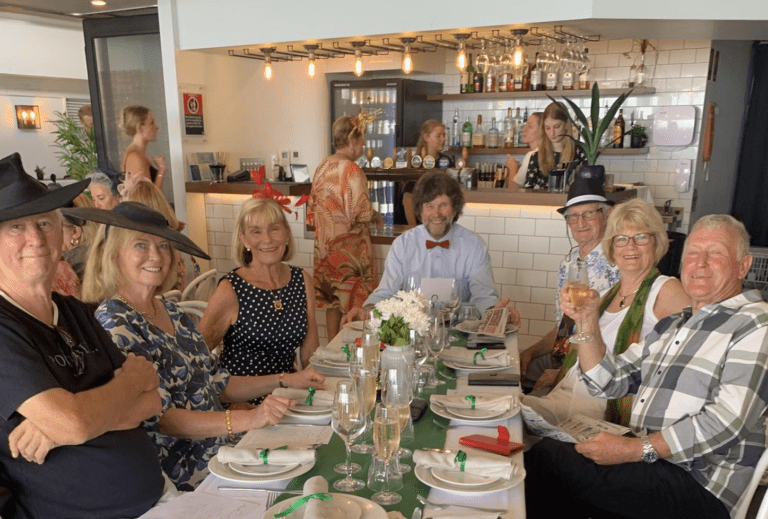 A group of smiling people seated around a table in a restaurant, with a server at the bar in the background